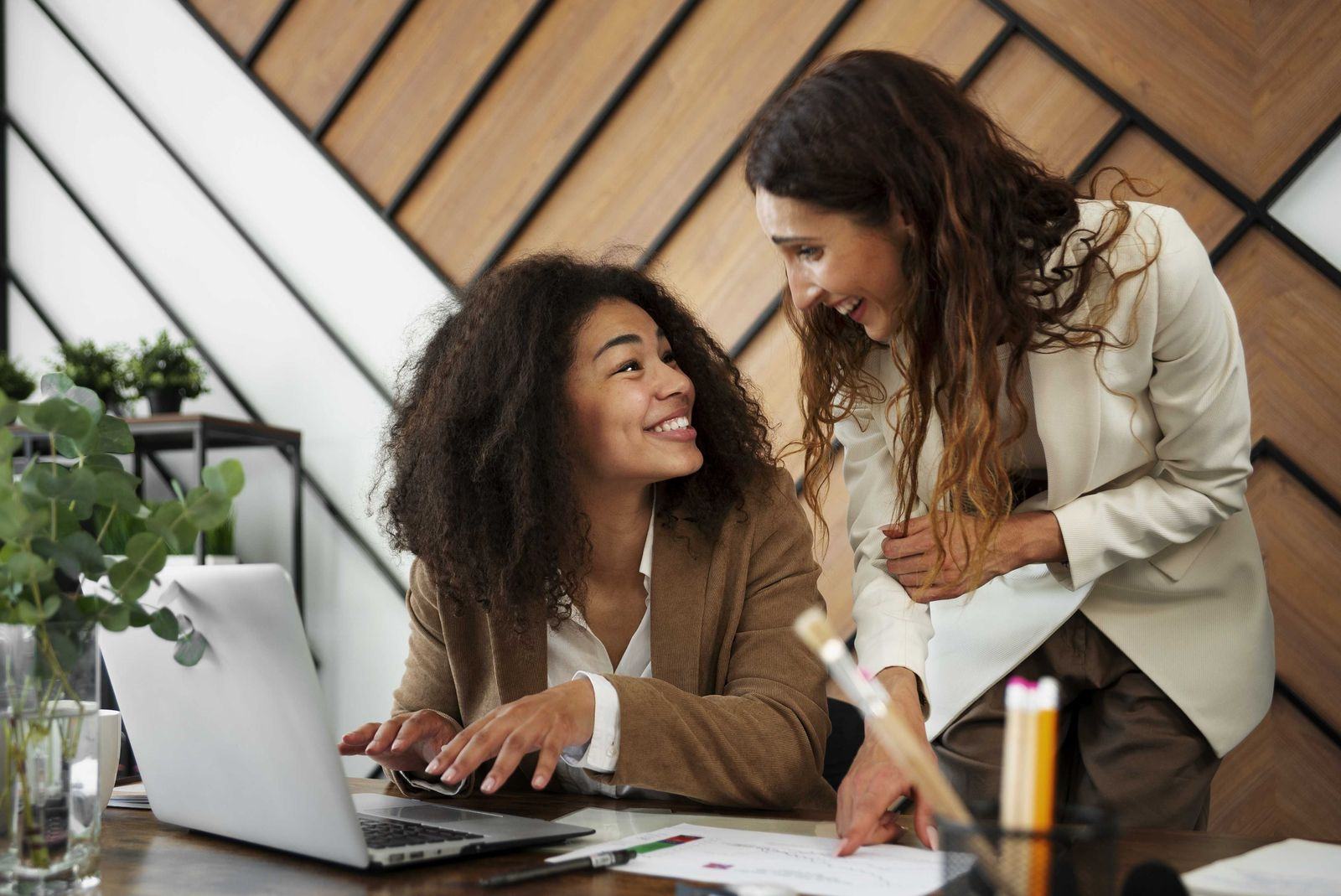 Two colleagues smiling over a laptop in a wood-panelled office